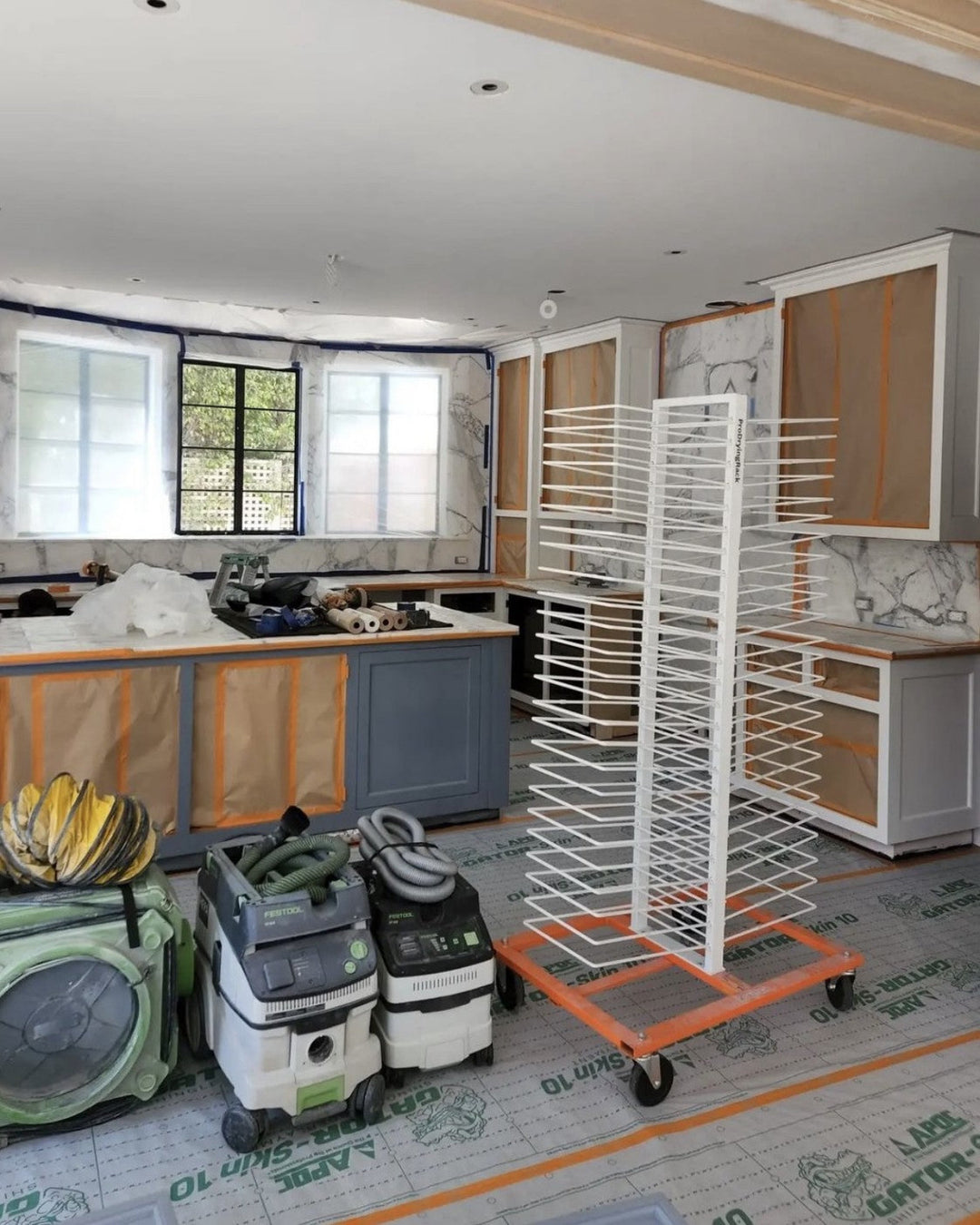 Kitchen under renovation with cabinets, countertops, cleaning equipment, and a PaintLine 50-shelf cabinet door drying rack.