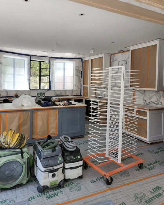 Kitchen under renovation with cabinets, countertops, cleaning equipment, and a PaintLine 50-shelf cabinet door drying rack.