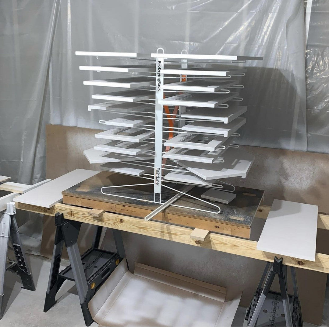 Stack of cabinet doors on a 20-shelf drying rack, sitting on to of a workbench