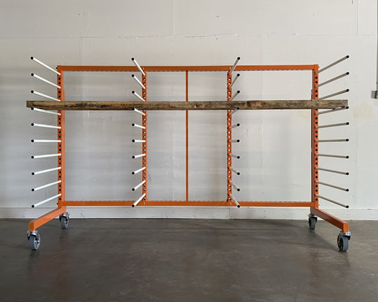 Orange metal rack with 4 towers and 10 levels of white shelves, holding a piece of long plywood