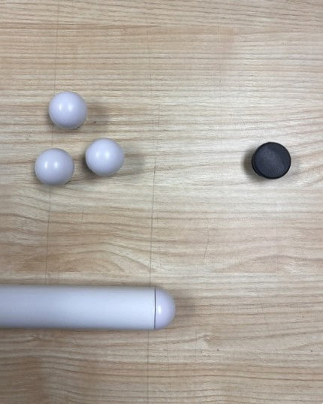A close up image of a white shelf tube, with three white shelf caps and one black shelf cap, sitting on a wooden table.