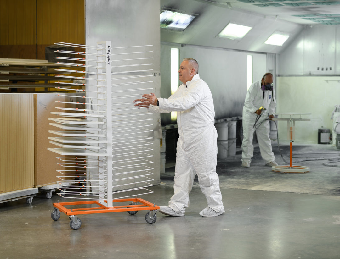 Two workers in a workshop pushing a drying rack with cabinet doors.