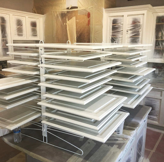 Stack of cabinet doors on drying racks sitting on a countertop
