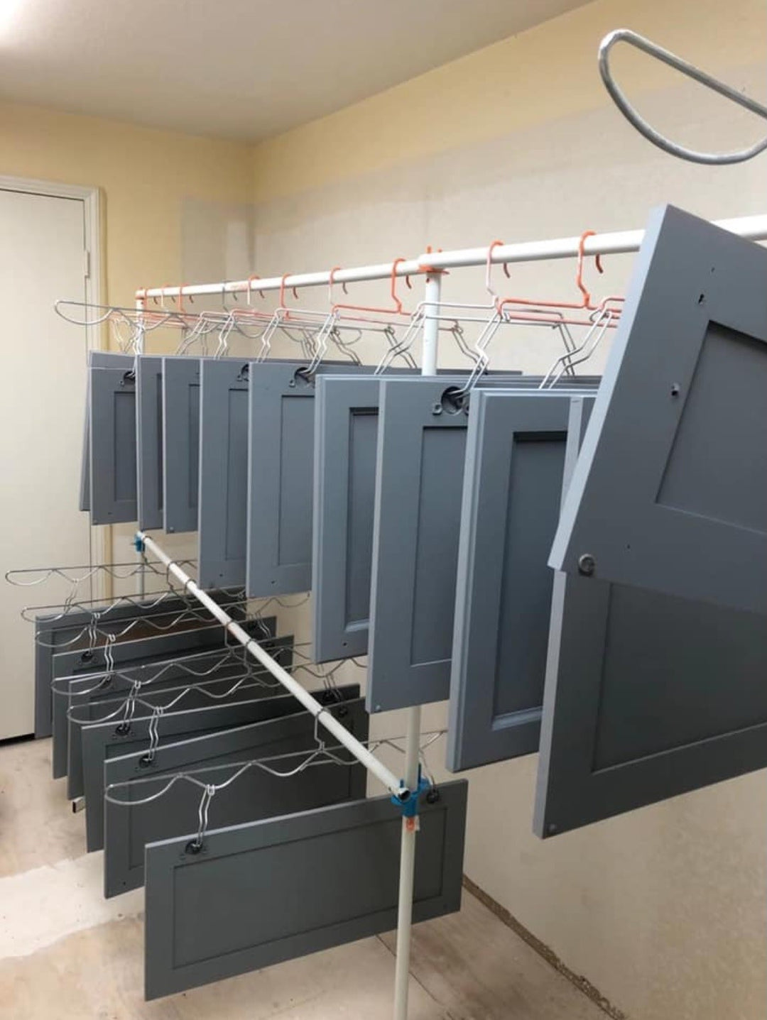 PRODRYINGRACK SD (PSDR) SERIES WAVE HANGERS, STANDARD HANGERS, EFC HINGE HOOKS, AND 2ND TIER CONNECTORS IN USE WITH GRAY CABINET DOORS HANGING VERTICALLY TO DRY