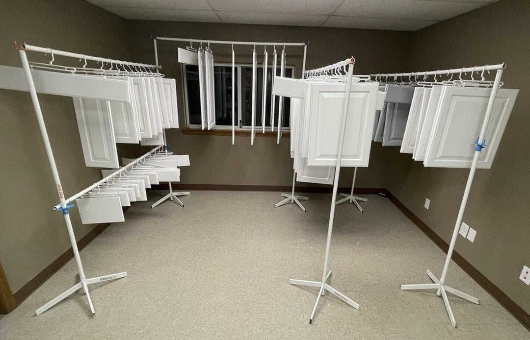 Room with white metal drying rack bars holding cabinet doors on multiple levels against a neutral wall