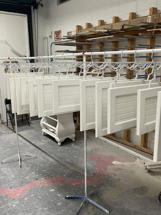 White cabinet doors hanging on metal hangers on a white stand in a warehouse setting
